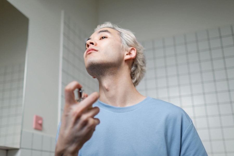 A man spraying perfume on his neck.